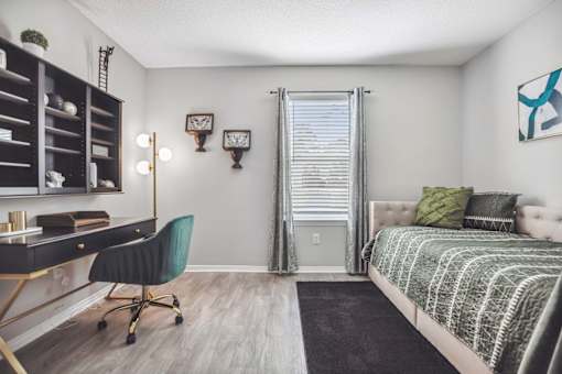 A room with a desk, chair, and bed.