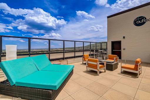 A patio with a couch, chairs, and a table with a view of the sky.