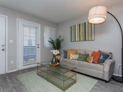 A living room with a glass coffee table and a striped picture on the wall.