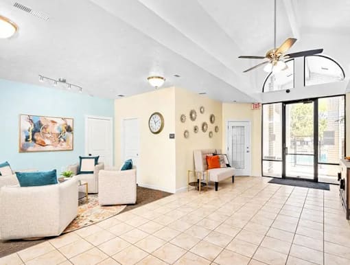 A living room with a white couch, a painting, a clock, and a fan.