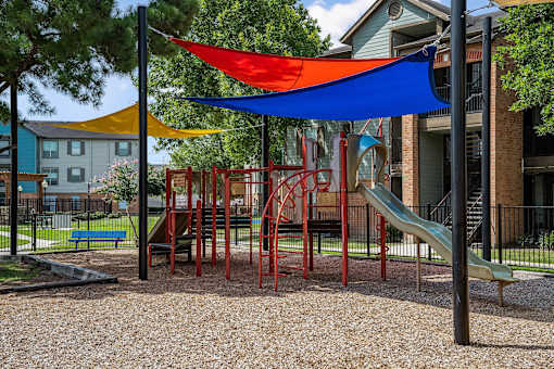 A playground with a red slide and a blue and yellow shade structure.
