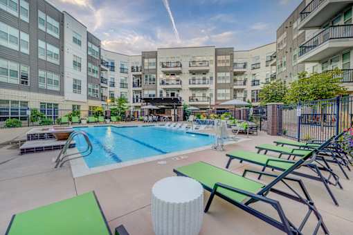 A swimming pool surrounded by lounge chairs and umbrellas in a courtyard.