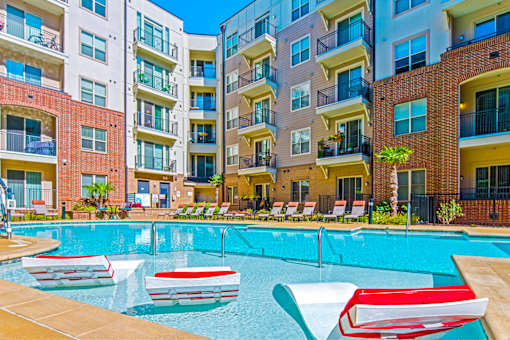 A pool with red and white chairs in front of apartment buildings.