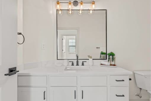A white bathroom with a sink, mirror, and lights.
