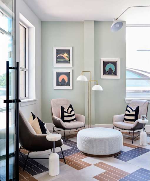 A living room with a chair, ottoman, and pictures on the wall.