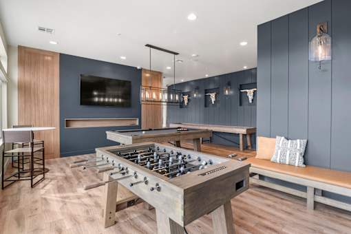 A foosball table is in the middle of a room with a bench and a television.