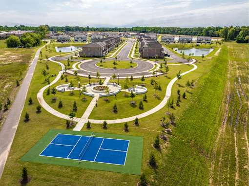 A tennis court is surrounded by a green lawn and a pond.