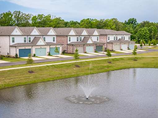 A fountain in the middle of a pond in front of a row of houses.
