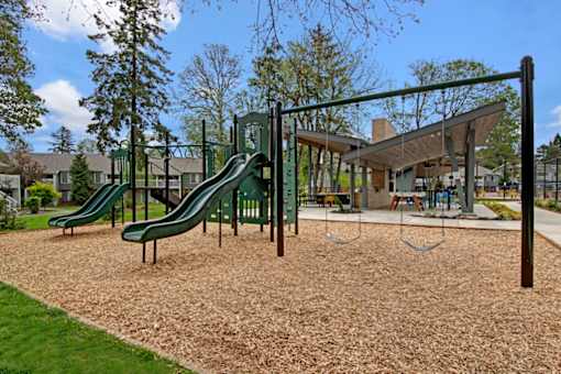 A playground with a green slide and brown sand.