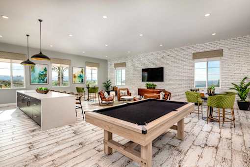 A pool table is in the middle of a room with a bar and a television.