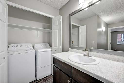 A white laundry room with a sink, mirror, and washer and dryer.