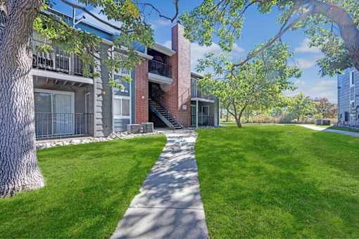 A tree-lined walkway leads to a brick building.