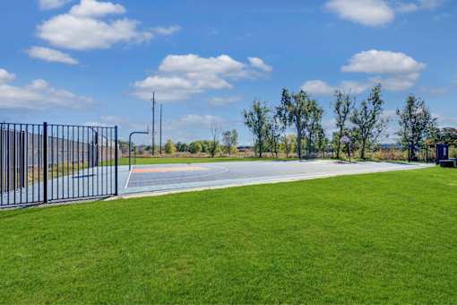 A black fence surrounds a green field with a road and trees in the distance.