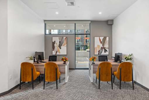 A room with a desk and chairs with a painting on the wall.