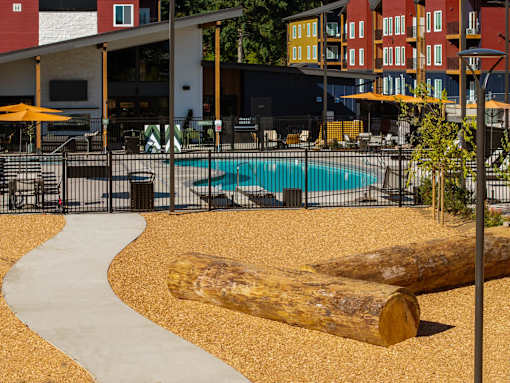 A large log sits in the middle of a sandy area in front of a pool.