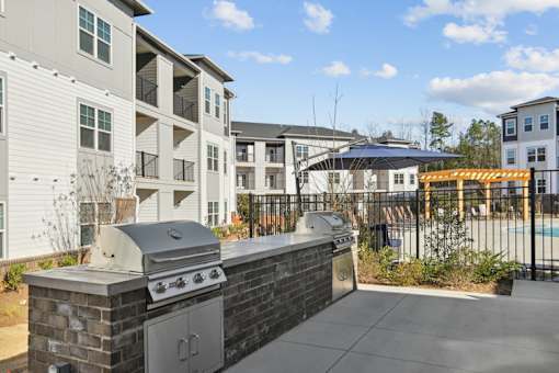 A BBQ grill is on a patio in front of apartment buildings.