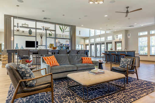 A residential lounge area with chairs, a center table, a grey couch, and an island countertop with barstool chairs at Parkstone at Knightdale apartments for rent in Knightdale, NC.
