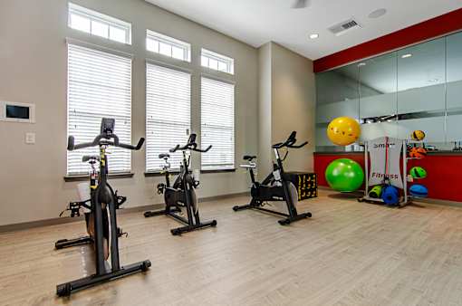 Three exercise bikes are lined up in a room with a red wall and a mirror.