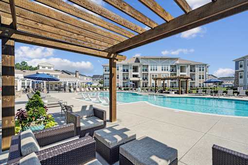 A pool area with a wooden pergola and lounge chairs.
