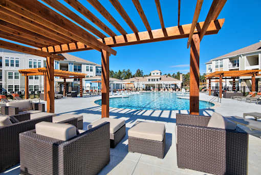 A pool area with a wooden pergola and wicker chairs.