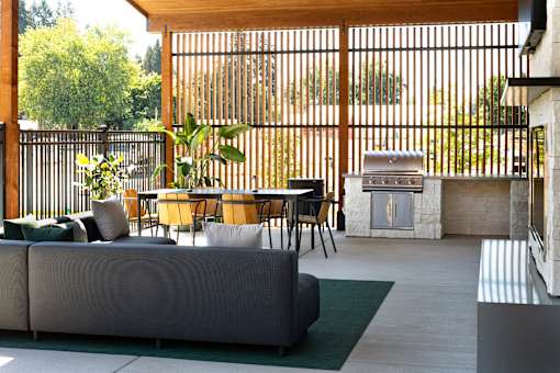 A patio with a grey couch, a table and chairs, and a fireplace.