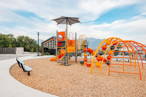 A playground with orange and black equipment and a brown bench.