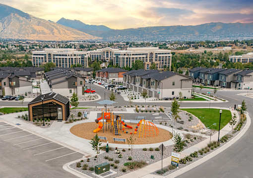 A playground with a slide and a play structure is surrounded by houses and a large building in the background.
