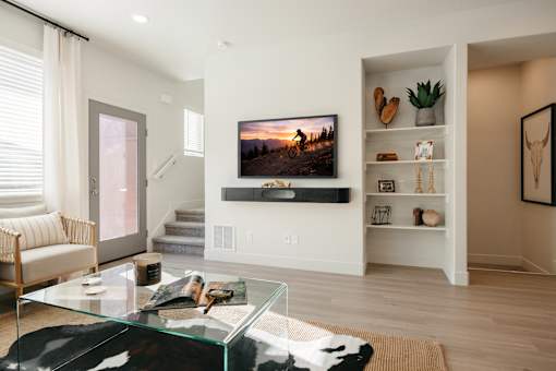 A modern living room with a glass coffee table and a flat screen TV mounted on the wall.