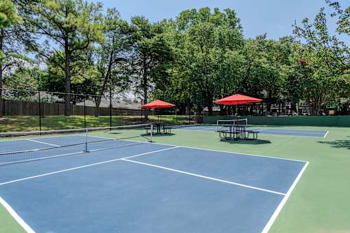A tennis court with a net and two red umbrellas.