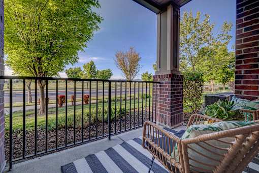 A patio with a black and white striped rug, a wicker chair, and a black metal fence.