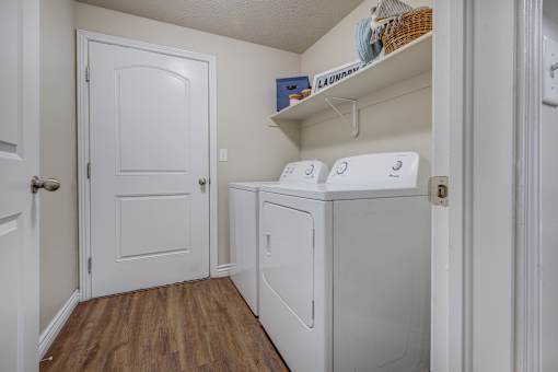 A white door is on the left of a small laundry room.