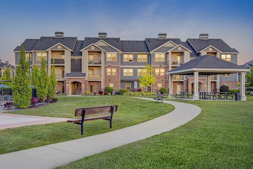 A large apartment complex with a grassy area in front and a bench on the sidewalk.