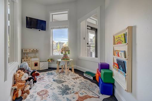 A room with a rug, a table, a chair, a shelf with books, and a window.