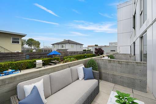 A modern outdoor seating area with a concrete wall and a grey couch.