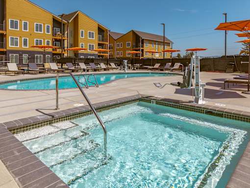A swimming pool in front of a building with orange umbrellas.