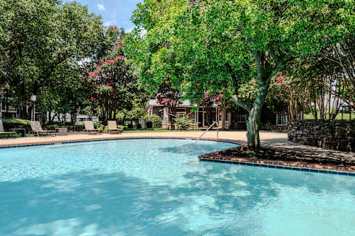 A swimming pool surrounded by trees and chairs.