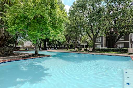 A swimming pool surrounded by trees and a building in the background.