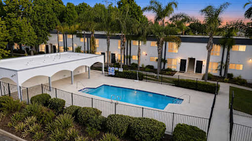 A pool surrounded by a black fence and bushes in front of a building.