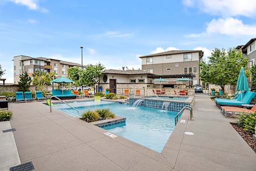 A swimming pool with a waterfall and a building in the background.