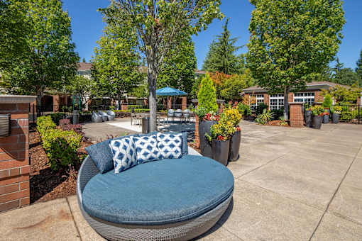 A blue cushioned chair with a pillow is in the foreground of a sunny courtyard.