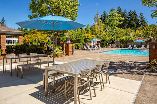 A table and chairs set is arranged on a patio with a pool in the background.