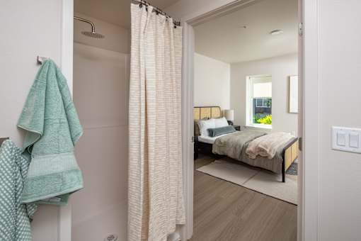 A bathroom with a towel hanging on the wall and a bed in the background.
