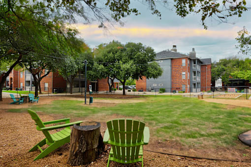A park with a green chair and a tree stump in the foreground.