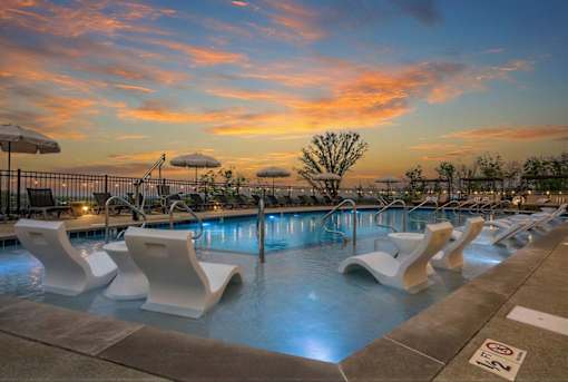 A pool with white chairs and a sunset in the background.