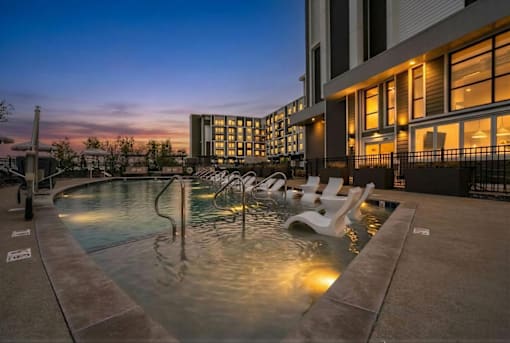 A pool with chairs around it is lit up at dusk.