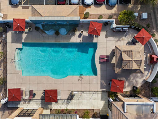 An aerial view of a pool surrounded by red umbrellas and chairs.