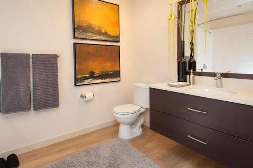 A bathroom with a toilet, sink, and two paintings on the wall.