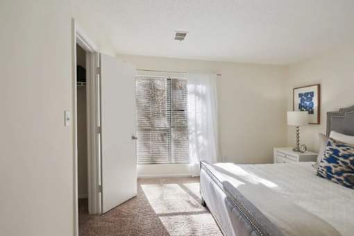 A bedroom with a bed, a nightstand, and a window with blinds.