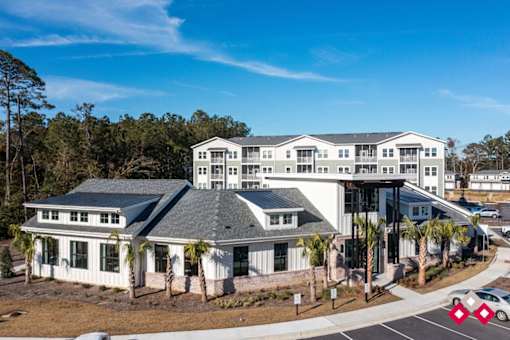 A large white building with a grey roof is surrounded by trees.