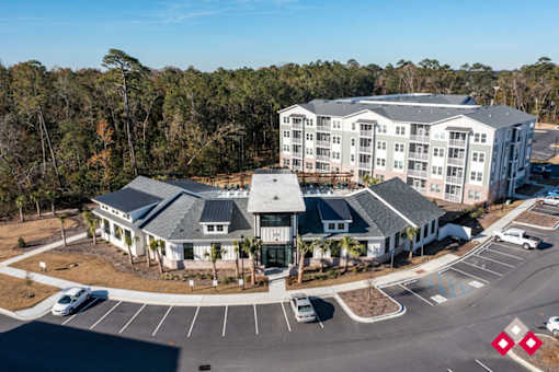 A large white building with a grey roof is surrounded by a parking lot.